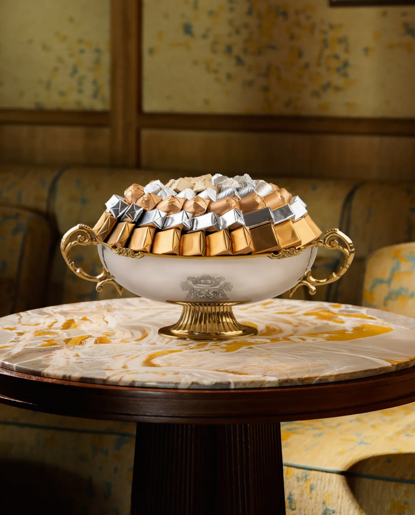 Coupe blanche à anses dorées garnie de chocolats or, argent et bronze sur une table en marbre