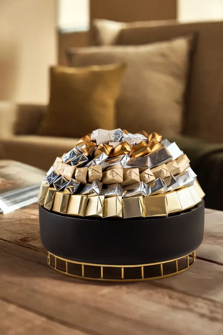 Boîte cylindrique noire et dorée couronnée de chocolats or et argent sur une table en bois